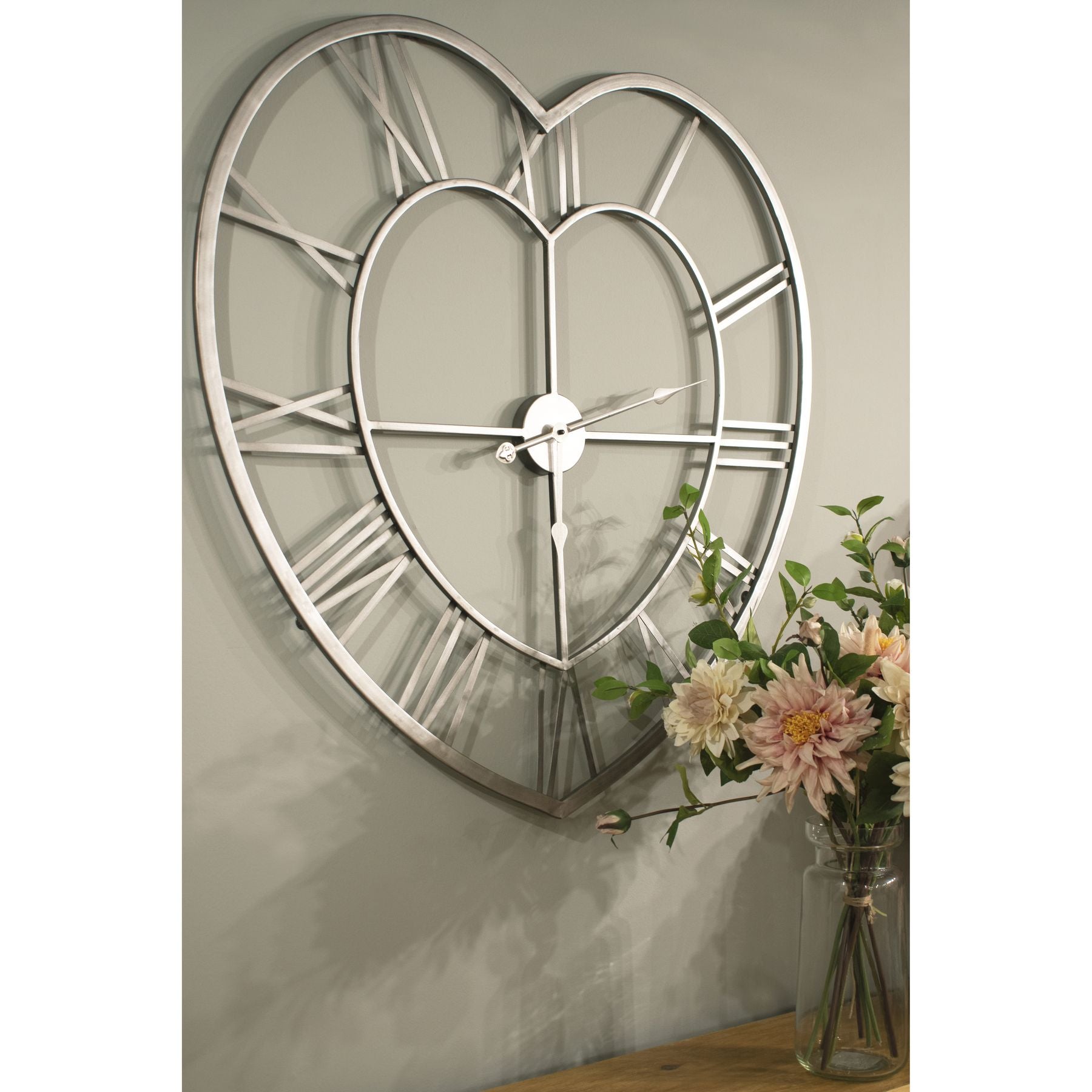 A unique shaped clock featuring a heart design, the wall clock has been handcrafted beautifully to create its curves. This Heart Skeleton Wall Clock is large in size so quite the statement piece, it'll sit comfortably in any setting and help brighten it up. Charming with a minimalistic aesthetic, it features a silver metal frame with roman numeral dials and hands.

Dimensions in cm H89 X W89 X D4